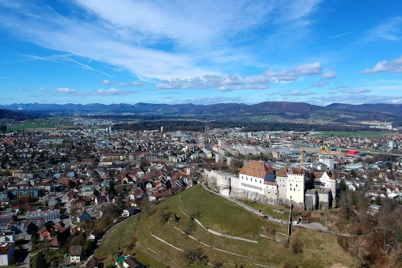 Schloss Lenzburg auf seinem Hügel über der Stadt, dahinter die Ebene und bewaldete Hügelzüge