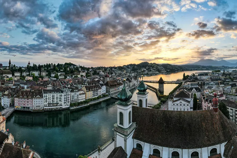 Die Türme der Jesuitenkirche über der Reuss, dahinter die Altstadt von Luzern und die Kapellbrücke bei Sonnenaufgang